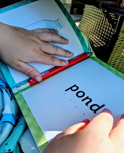 A child reading the word pond with sound dots in a Read and See book.